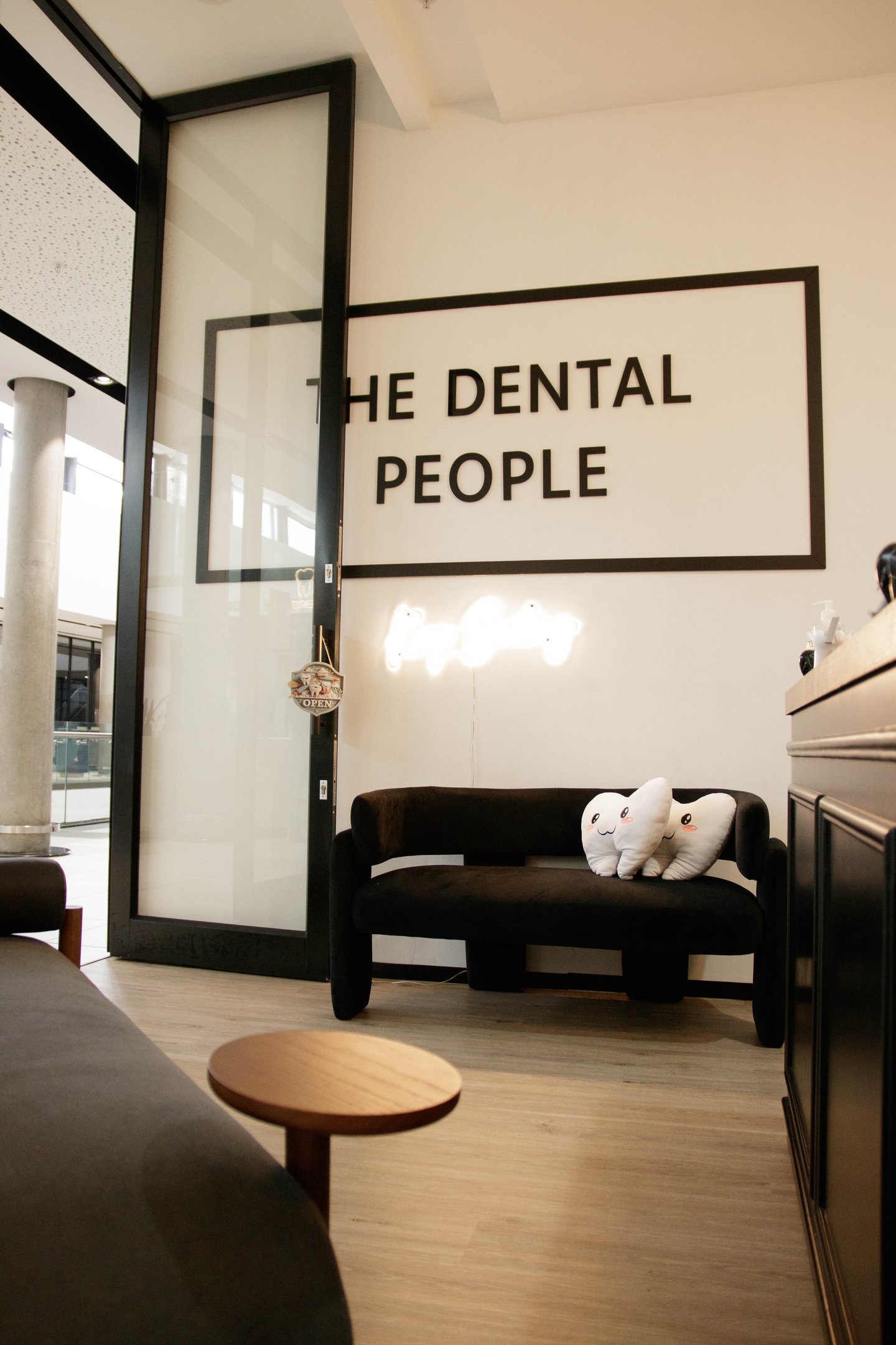 The Dental People office waiting area with tooth-shaped pillows on a black couch and neon sign.